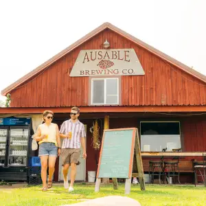 A man and woman walk past a red barn turned into a brewery. 