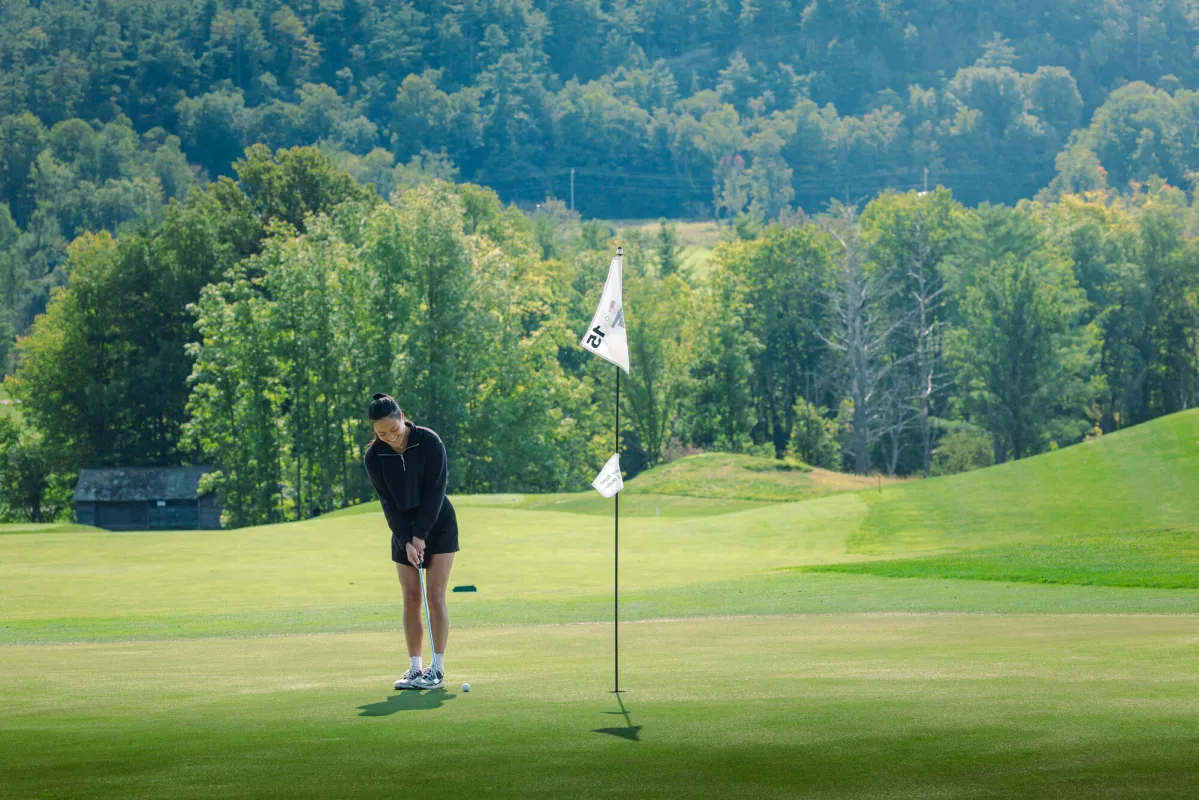 A woman puts a golf ball into a hole on a golf course.