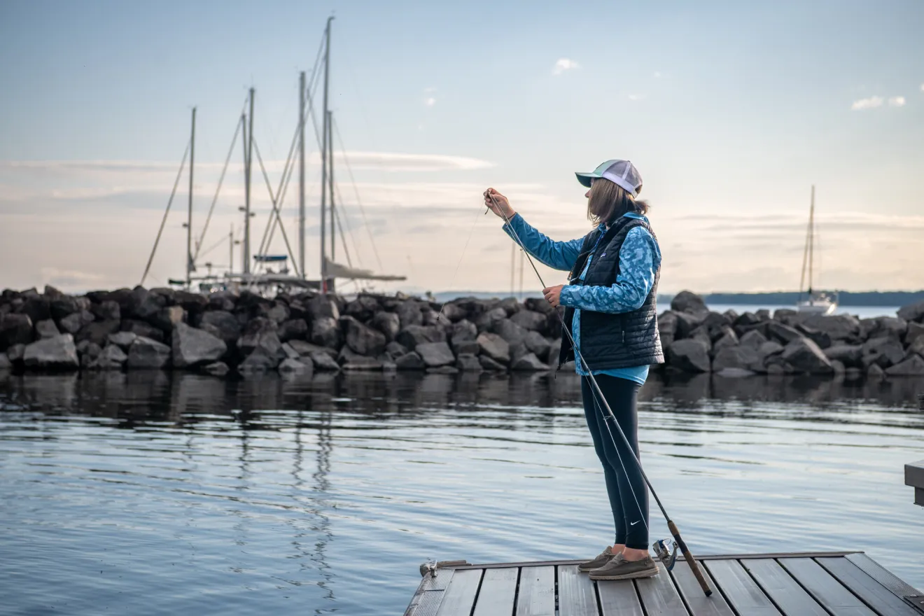 A woman prepares a fish hook on a line while standing on a pier.