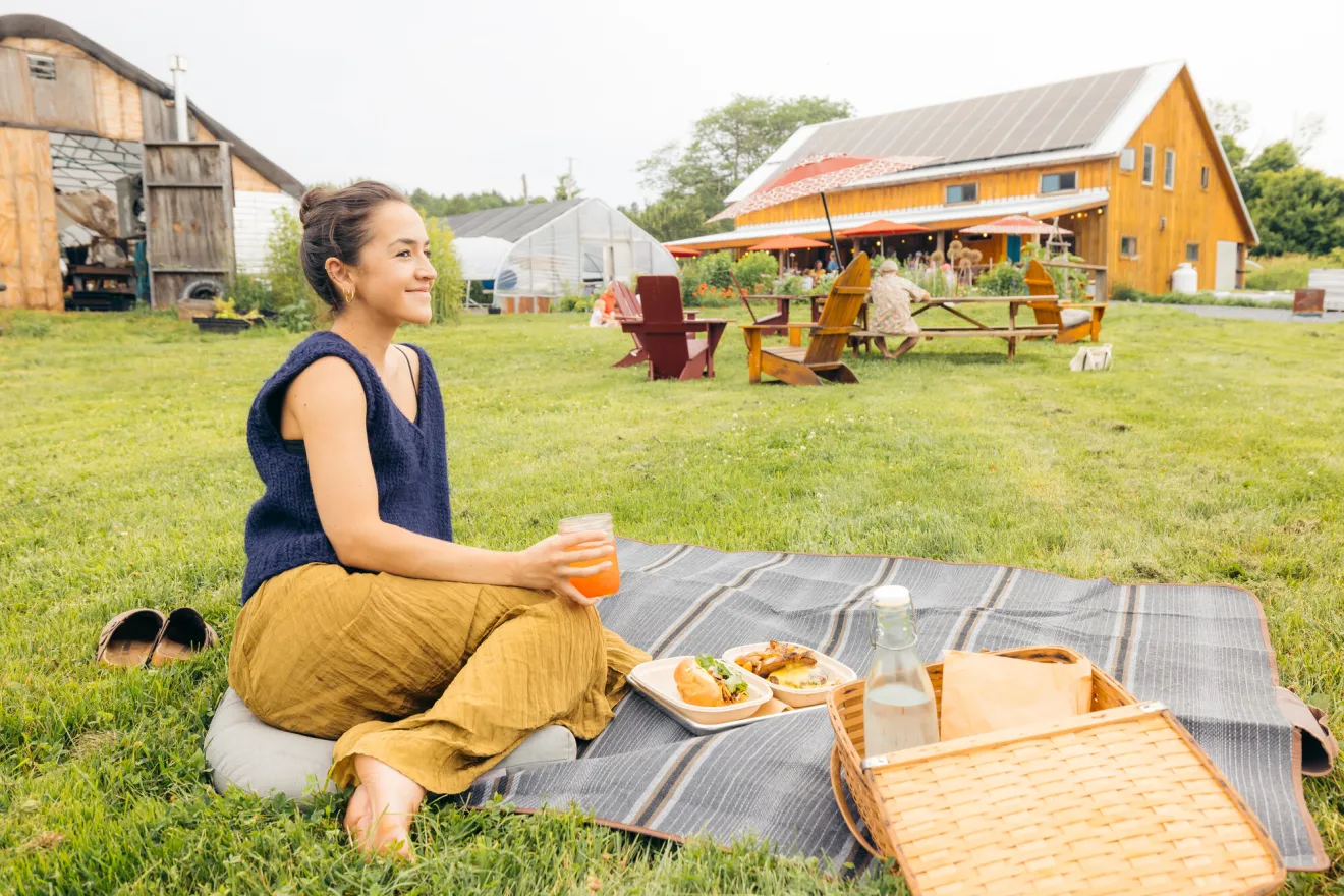 A woman dines on a sandwich and picnic outside a farm-style bistro.