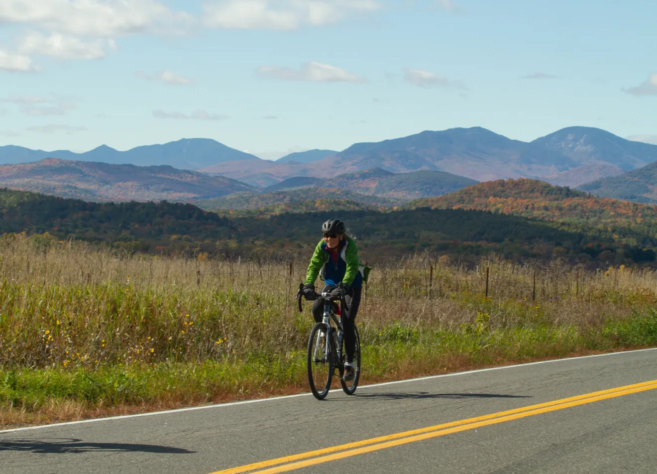 A woman rides a bike on a mountain road in fall.