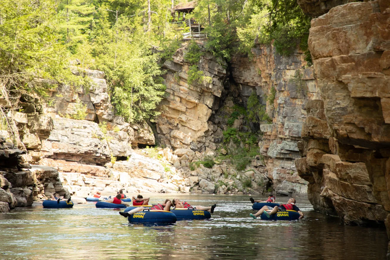 A group of adults float on large inner tubes down a rocky chasm.