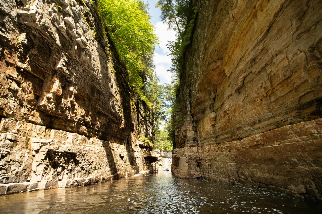 A rocky river chasm is viewed from the water, with tall, steep rock walls extending upward out of frame.