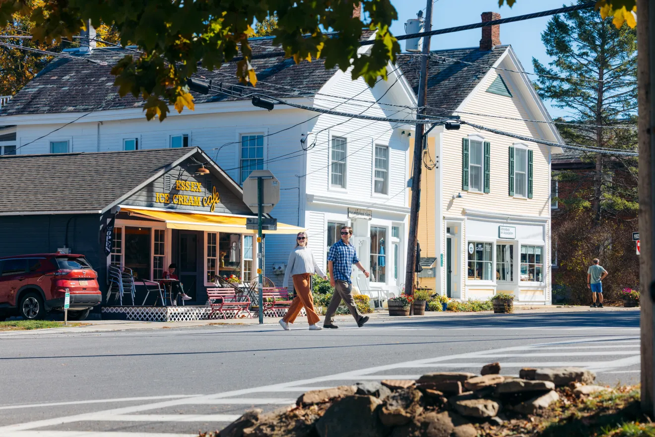 A man and woman walk across a road in the center of town in fall.