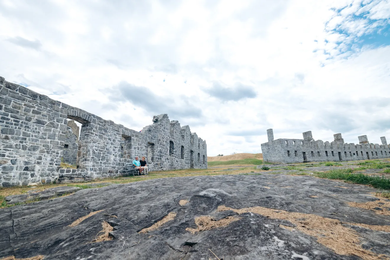 A man and woman explore fort ruins on a grassy hill.