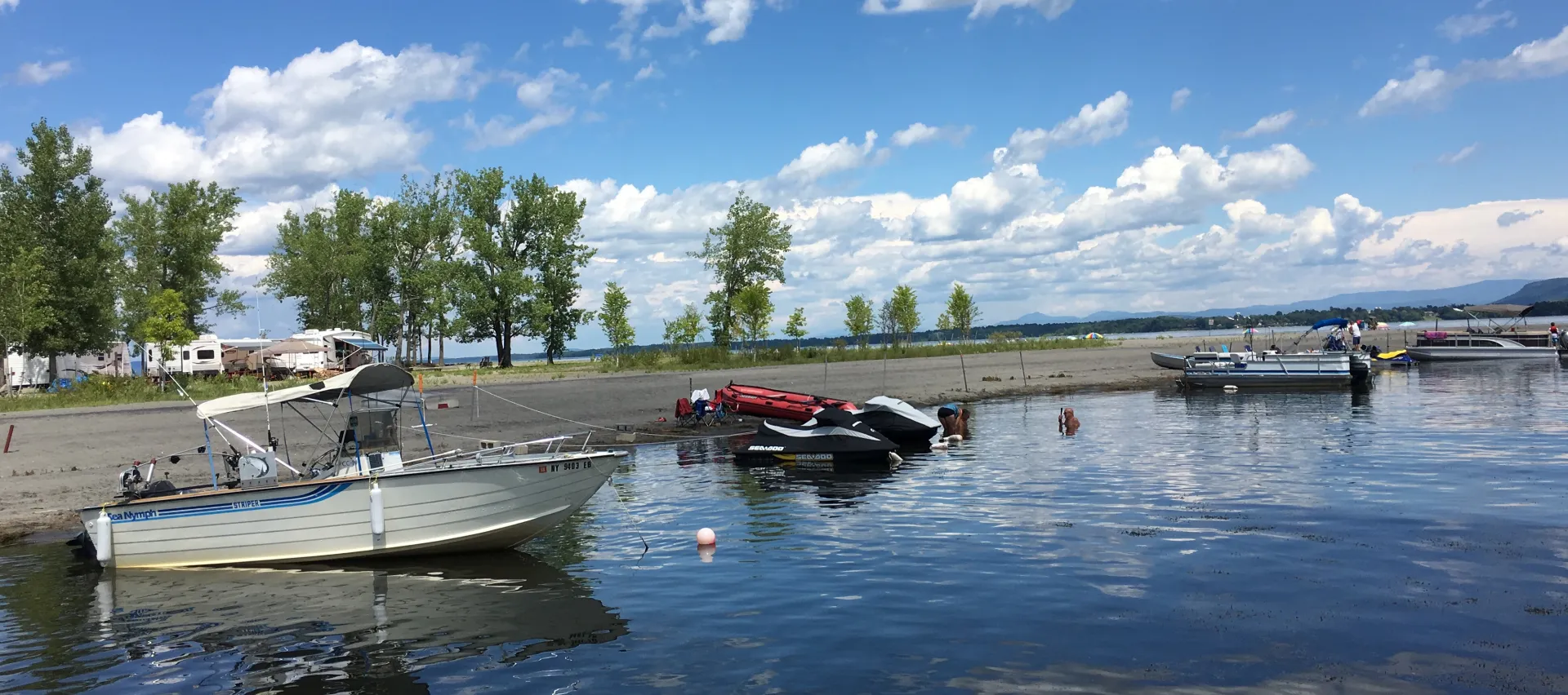 Boats and jet skis are moored near the sandy beach.