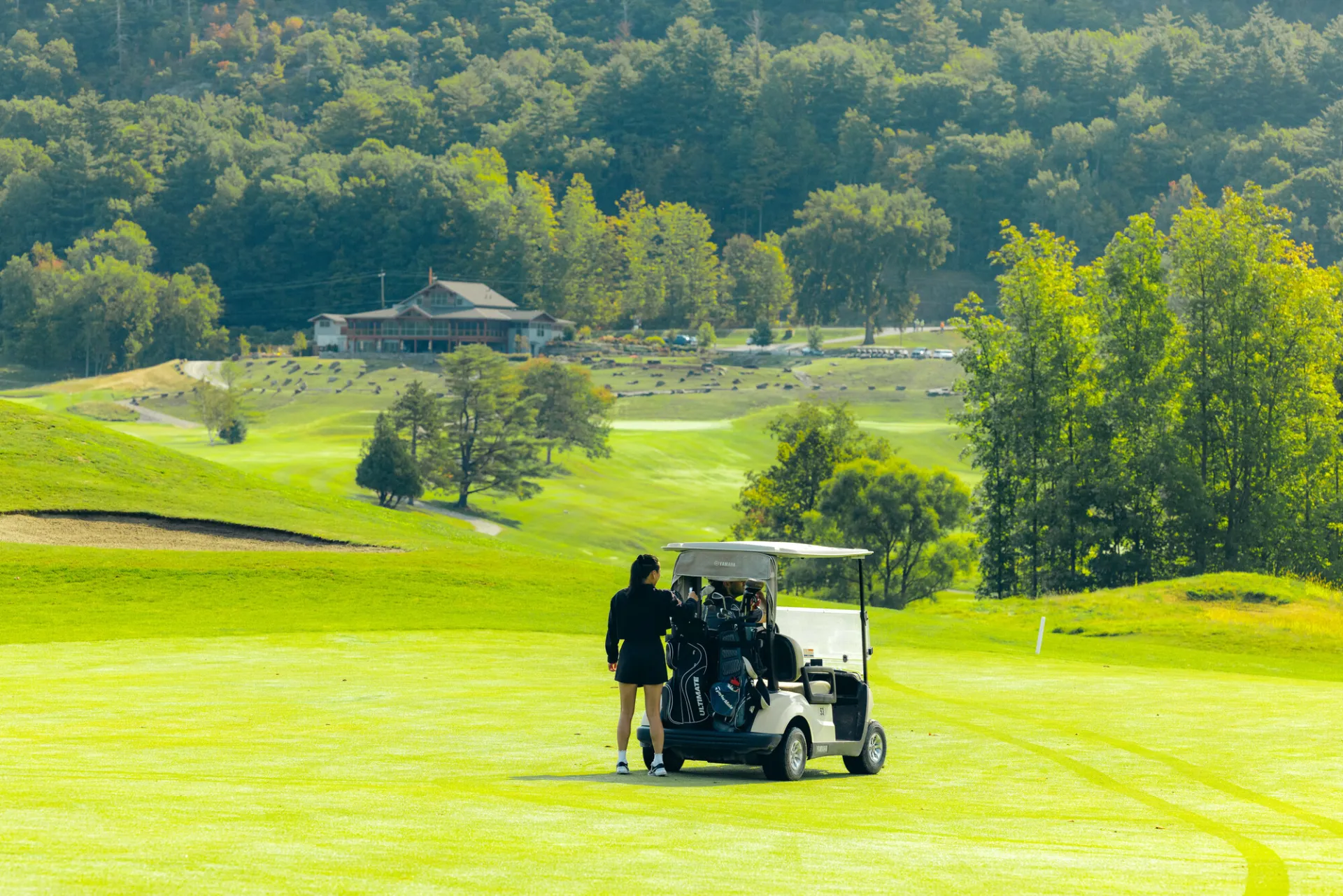 A woman grabs clubs from a golf cart. 