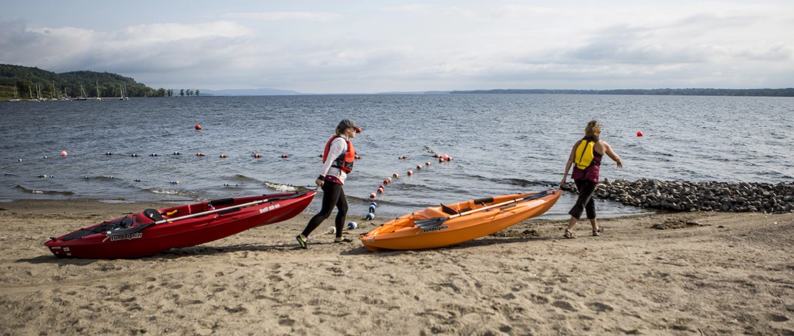 A woman pulls her kayak across the sand to the water.