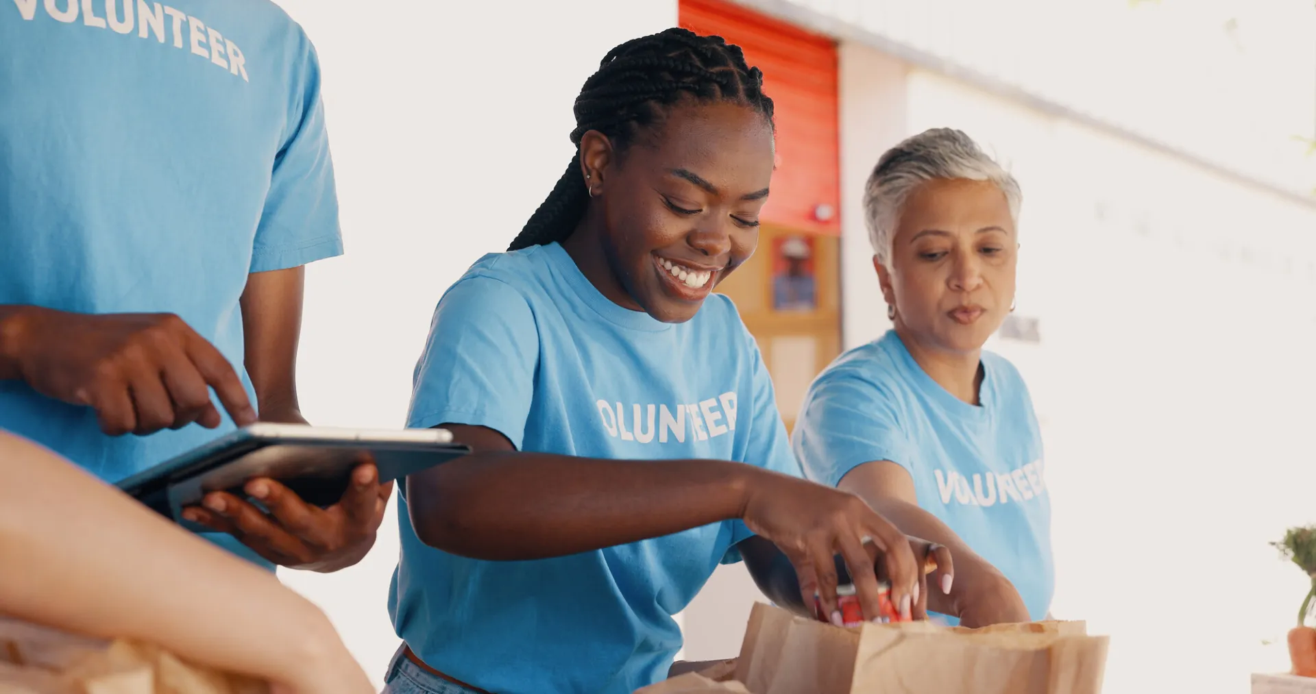 A group of volunteers in blue shirts help bag meals for people in need.