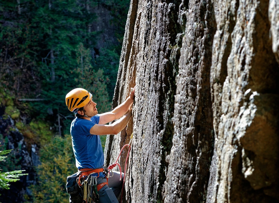 A man in a helmet, harness and ropes climbs a steep rock face.