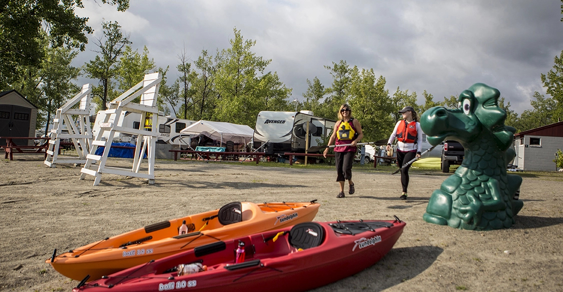 Two people with paddles walk toward their kayaks on the sandy shore.