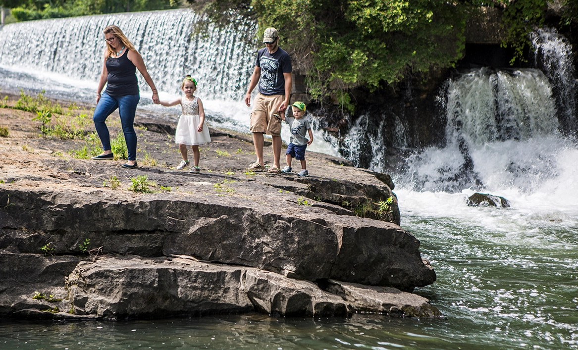 A man and woman climb rocks with their kids near a waterfall. 