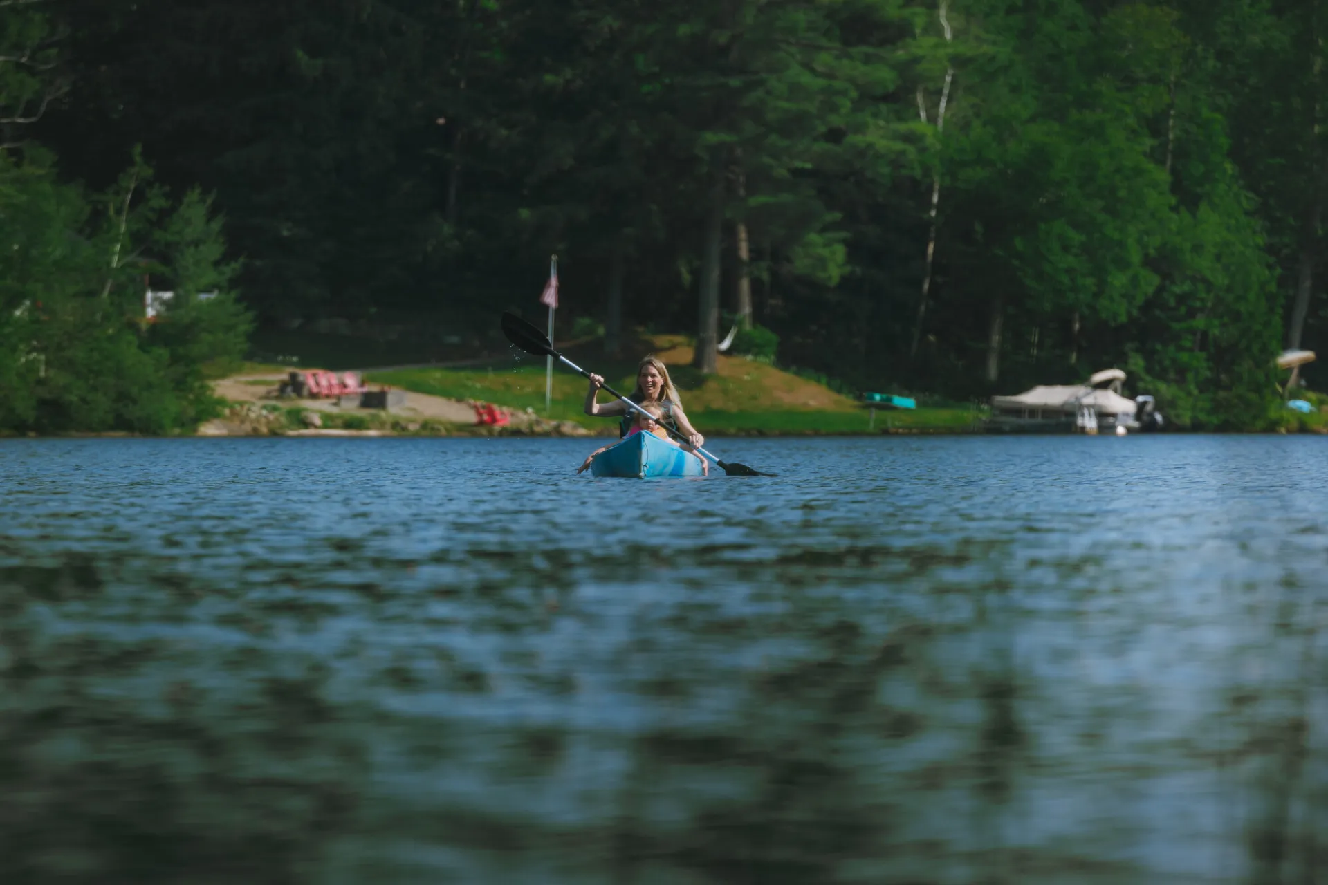 A woman paddles a kayak on a lake in summer.