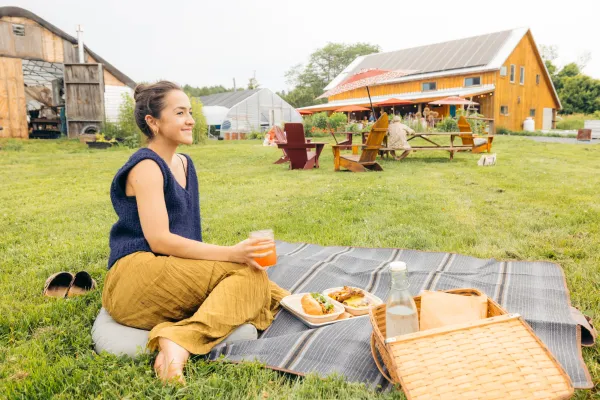 A woman sits on a picnic blanket at a brewery with farm fresh food. 