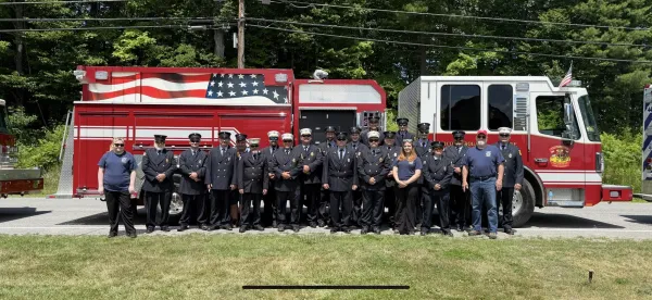 The volunteer fire fighters stand at attention in their full dress blues in front of a shiny fire engine