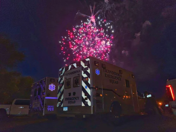The Ticonderoga Emergency Squad ambulance under a dark sky with red fireworks exploding above.