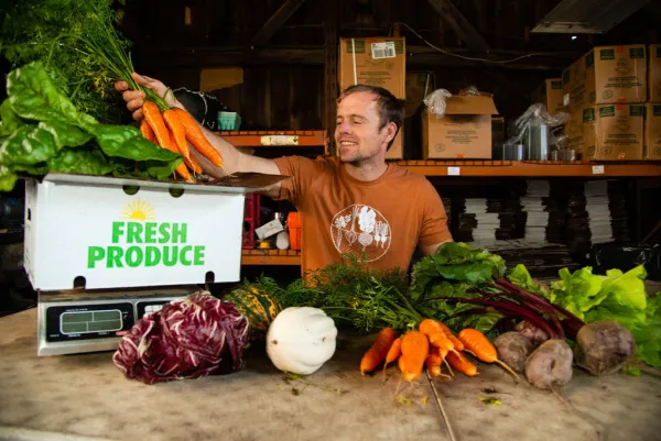 A man at a farm stand weighs a bundle of carrots.
