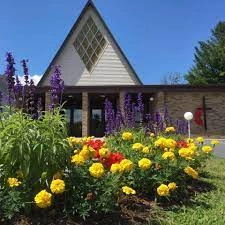 A building with tall peak and diamond shaped stained glass, withe lots of big yellow merigolds.