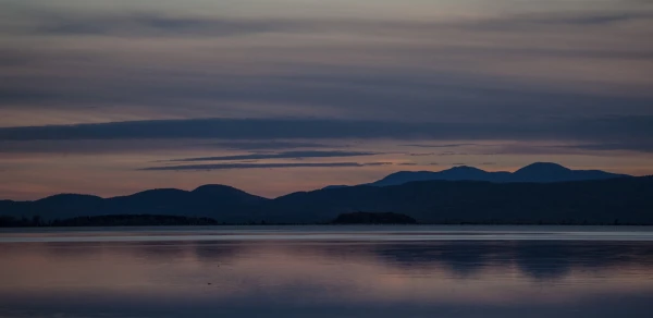 A view of the Adirondack Mountains over Lake Champlain at dusk.