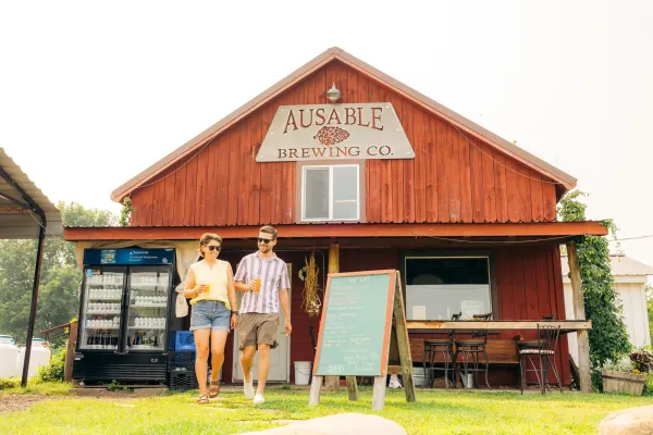 A man and woman walk past a red barn turned into a brewery. 