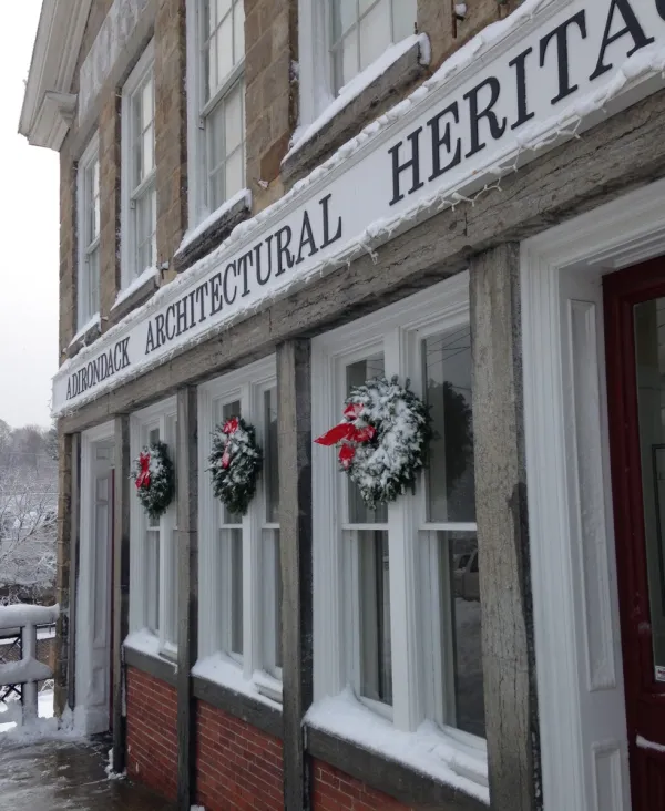 A tall stone building with white trim and winter wreaths with red bows that houses the Adirondack Architectural Heritage.