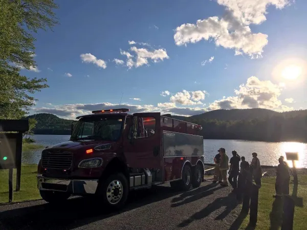 A fire truck by a lake surrounded by firefighters.