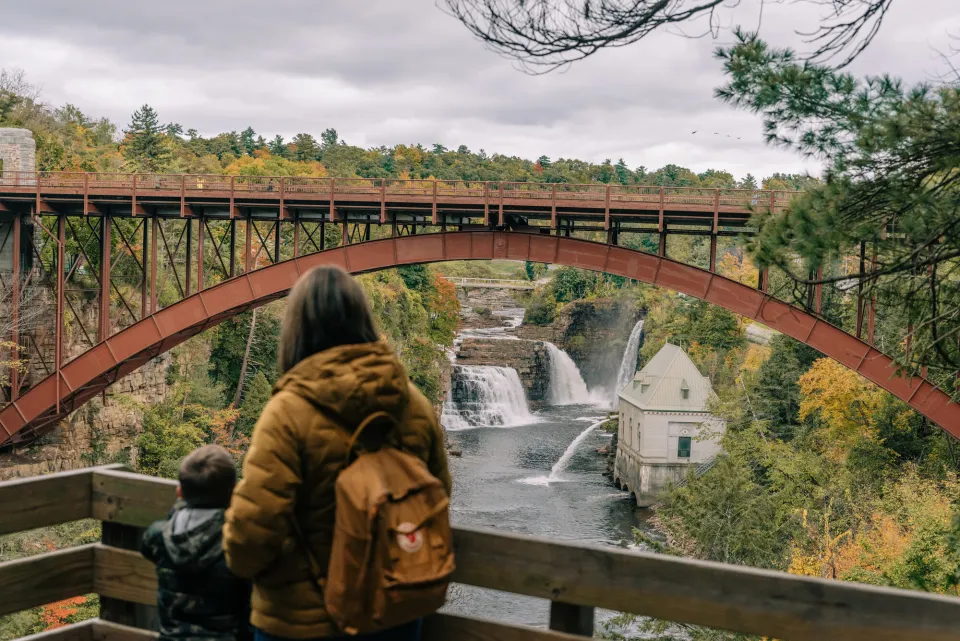 A woman and her young son look out at a waterfall behind a tall bridge.