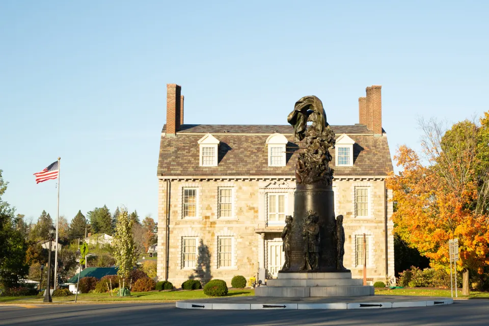 A three-story stone Federal mansion on a sunny fall afternoon. A large bronze statue is in front.