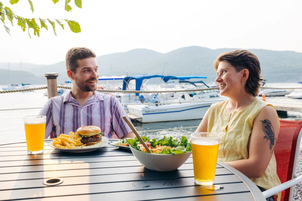 A man and woman sit at a lakeside restaurant and eat a burger and salad.