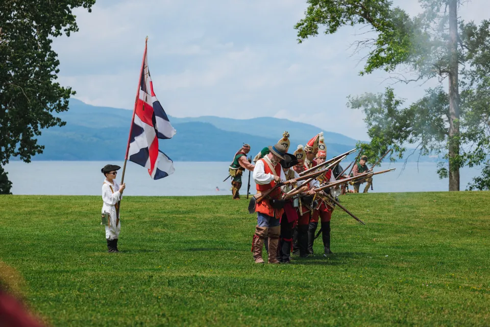 Reenactors in Revolutionary War costume participate in a lakeside battle.