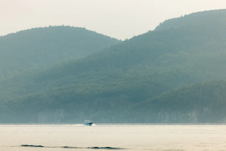 A boat glides across a lake with mountains behind it in summer.